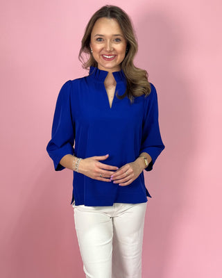 Woman wearing a blue blouse and white pants against a pink background