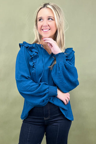Woman wearing a blue blouse with ruffled sleeves against a green background