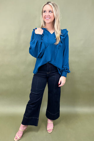 Woman wearing a blue blouse with ruffled sleeves and black pants on a green background