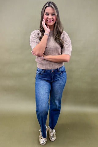 Woman wearing a beige sweater and blue jeans against a green background