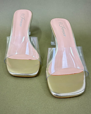 Gold high-heeled shoe with clear heel and against a green background