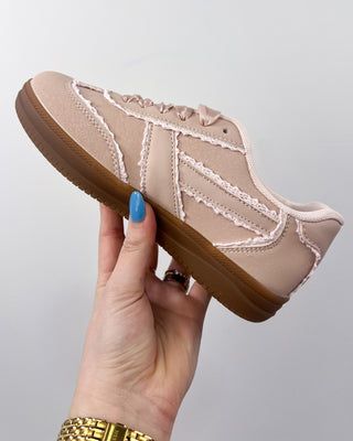 Beige sneaker with brown sole held by a hand against a gray background