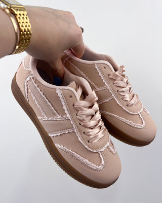 Beige sneakers with white accents held by a hand on a light gray background