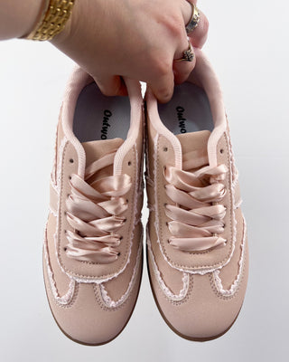 Pair of pink sneakers with satin laces held by a hand on a light background