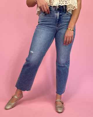 Person wearing blue jeans and a white lace top on a pink background