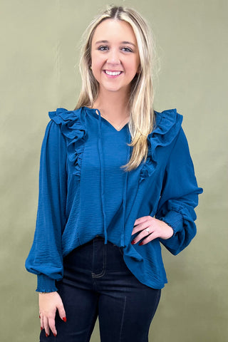 Woman wearing a blue blouse with ruffled sleeves against a green background