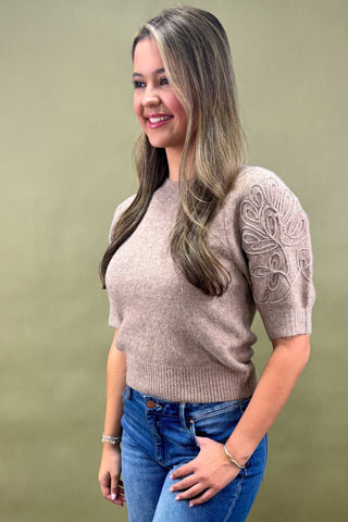Woman wearing a beige sweater with lace sleeves against a green background