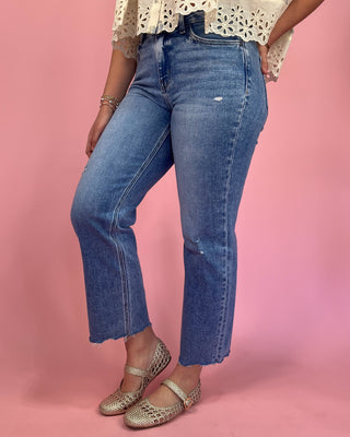 Person wearing blue jeans and a white lace top on a pink background