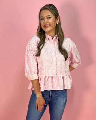 Woman wearing a pink patterned blouse and blue jeans against a pink background