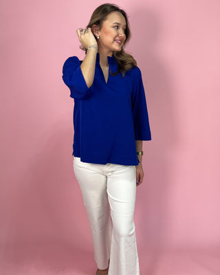 Woman wearing a blue top and white pants against a pink background