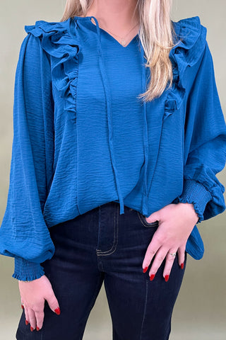 Woman wearing a blue blouse with ruffled sleeves against a neutral background