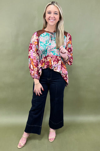 Woman wearing a colorful floral blouse and black pants against a green background