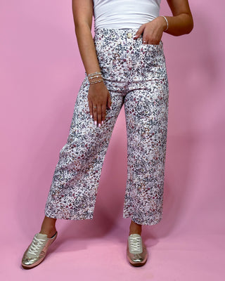 Person wearing floral pants and white sneakers on a pink background