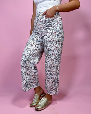 Person wearing floral pants and gold shoes on a pink background