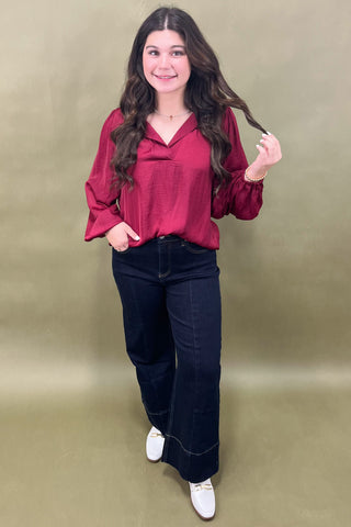 Woman wearing a red blouse and dark jeans against a beige background