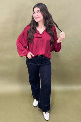 Woman wearing a red blouse and black pants against a green background