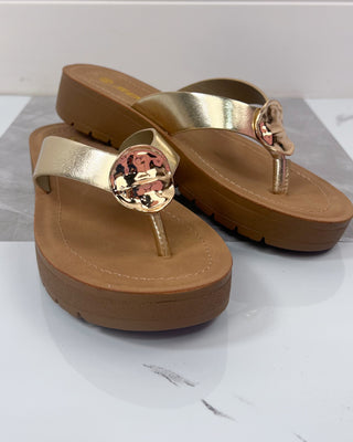 Pair of gold sandals with a decorative center on a white background
