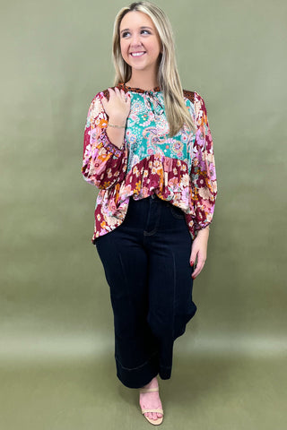 Woman wearing a colorful floral blouse and black pants against a green background
