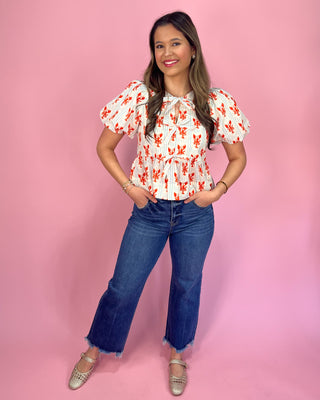 Woman wearing a floral blouse and jeans against a pink background
