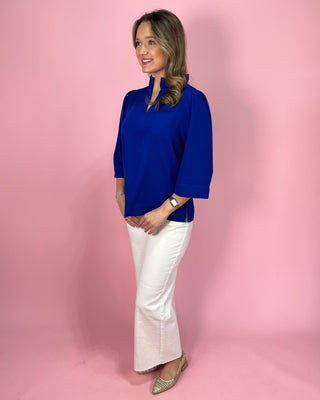 Woman wearing a blue top and white pants against a pink background