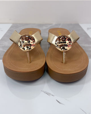 Pair of tan sandals with gold embellishments on a white background