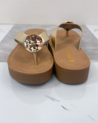 Pair of tan sandals with gold embellishments on a white background