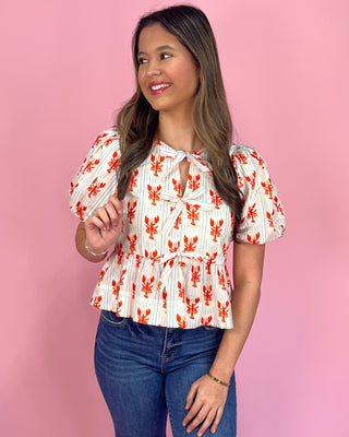 Woman wearing a white blouse with red patterns and blue jeans against a pink background