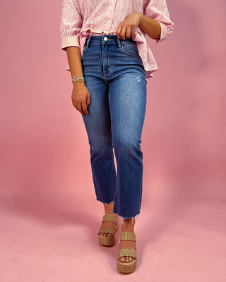 Person wearing blue jeans and a pink patterned shirt on a pink background