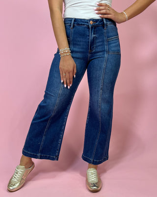 Person wearing blue jeans and gold sneakers on a pink background