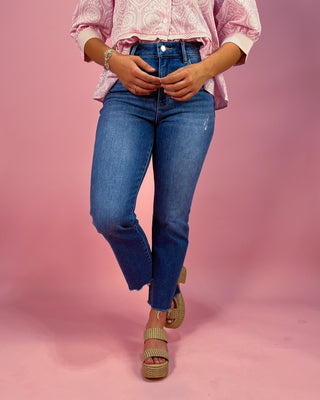 Person wearing blue jeans and a pink patterned shirt on a pink background