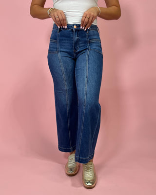 Person wearing blue jeans and a white top on a pink background