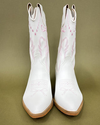White cowboy boots with brown soles on a green background