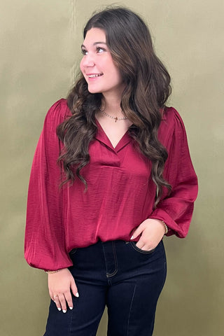 Woman wearing a red blouse and dark jeans against a beige background