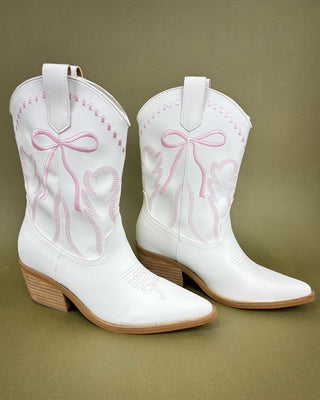 White cowboy boots with pink bows on a green background