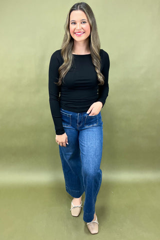 Woman wearing a black top and blue jeans against a green background