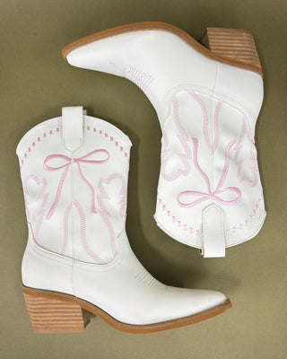 White cowboy boots with pink embroidery on a brown background