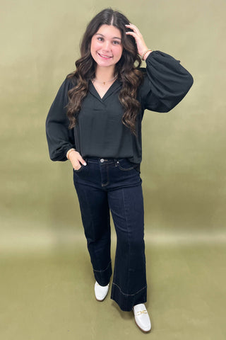 Woman wearing a black blouse and dark jeans against a green background
