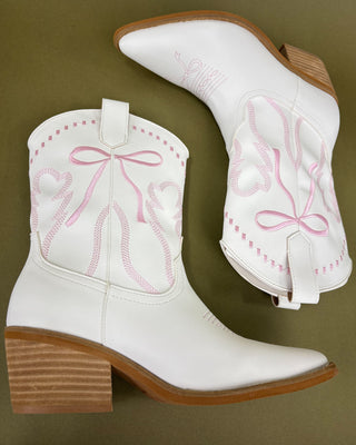 White cowboy boots with pink embroidery on a green background