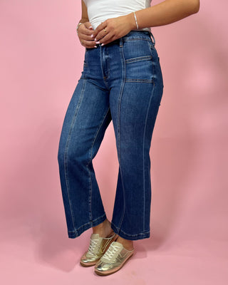 Person wearing blue jeans and gold shoes on a pink background