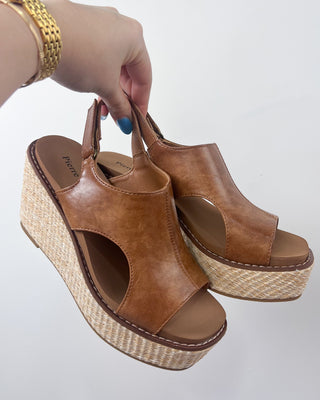 Brown wedge sandals with woven sole held by a hand on a light gray background