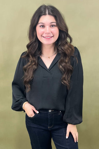 Woman wearing a black blouse and dark jeans against a green background