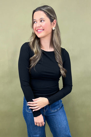 Woman wearing a black long-sleeve top and blue jeans against a green background