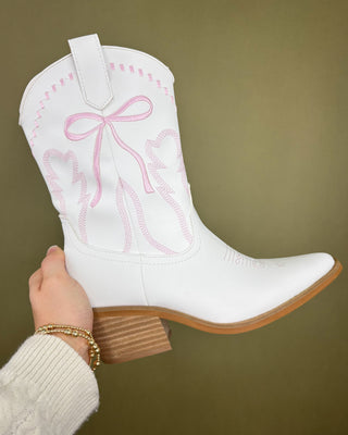 White cowboy boot with pink embroidery held by a hand against a green background