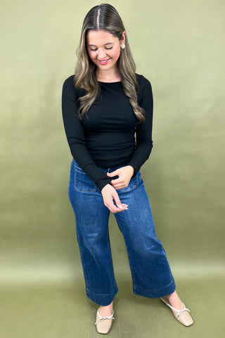 Woman wearing a black top and blue jeans against a green background