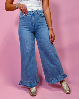 Person wearing blue wide-leg jeans with ruffled hem on a pink background