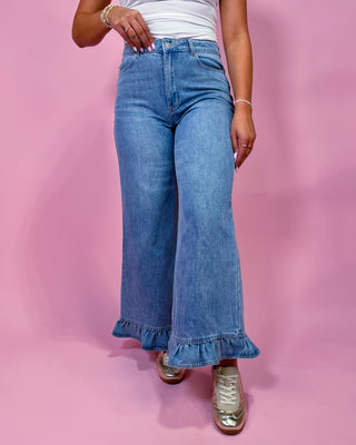 Person wearing blue jeans with ruffled hem on a pink background