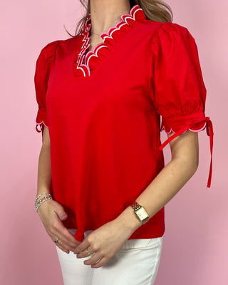 Red blouse with white trim worn by a person on a pink background