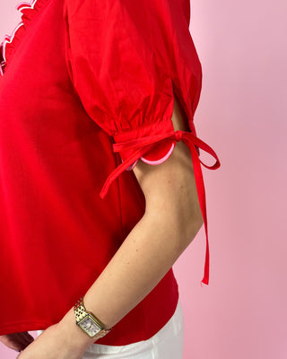 Red blouse with tied sleeves worn by a person on a pink background