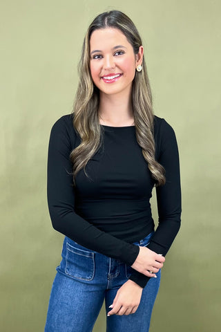 Woman wearing a black long-sleeve top and blue jeans against a green background
