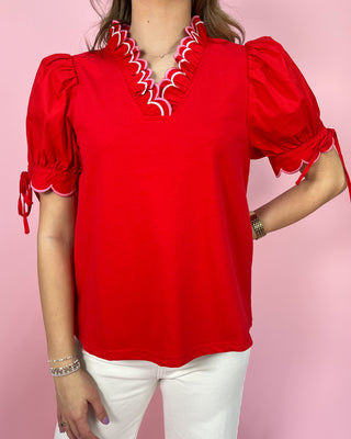 Red blouse with white trim worn by a person on a pink background